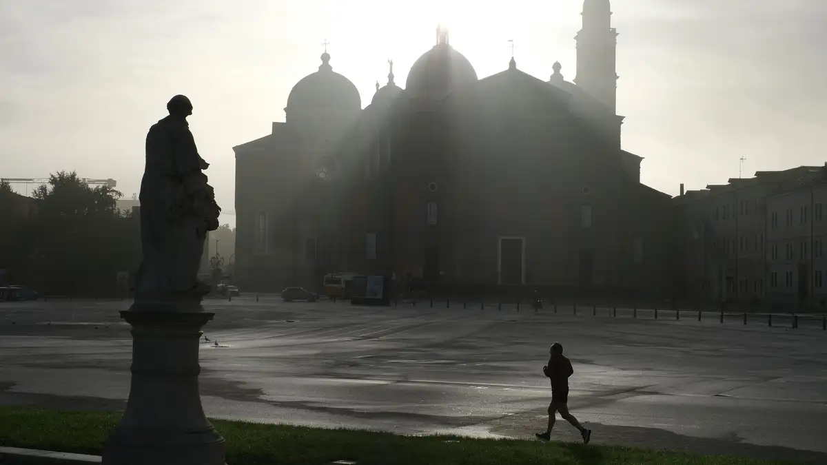 A jogger silhouettes against a misty European piazza with a historic church at sunrise.